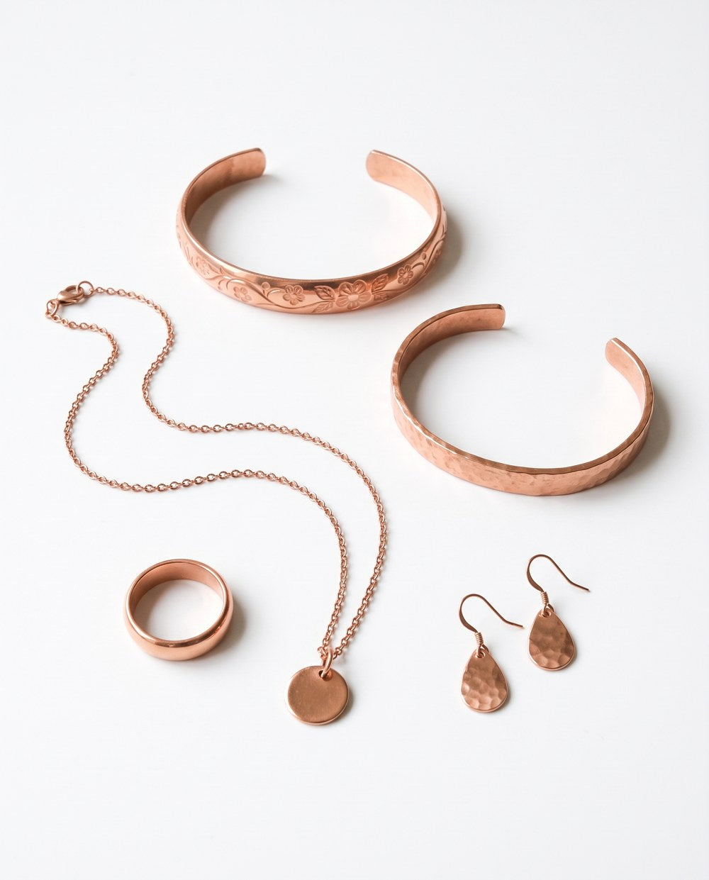 A row of solid copper cuffs and rings on white linen, one small price tag showing.